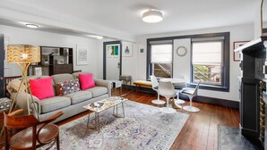 A living room with a sofa, coffee table, and chairs, a fireplace, and large windows. - Ground Level Apartment in City Center by Perry Lane Hotel (Savannah)