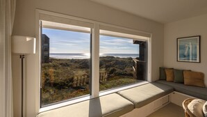 Quarto com uma grande janela com vista para o mar e paisagem distante.