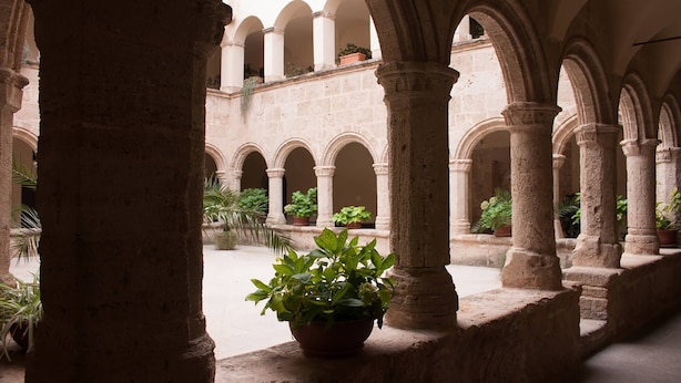 An interior courtyard with stone arches and potted plants. - San Francesco Heritage Hotel (Alghero)