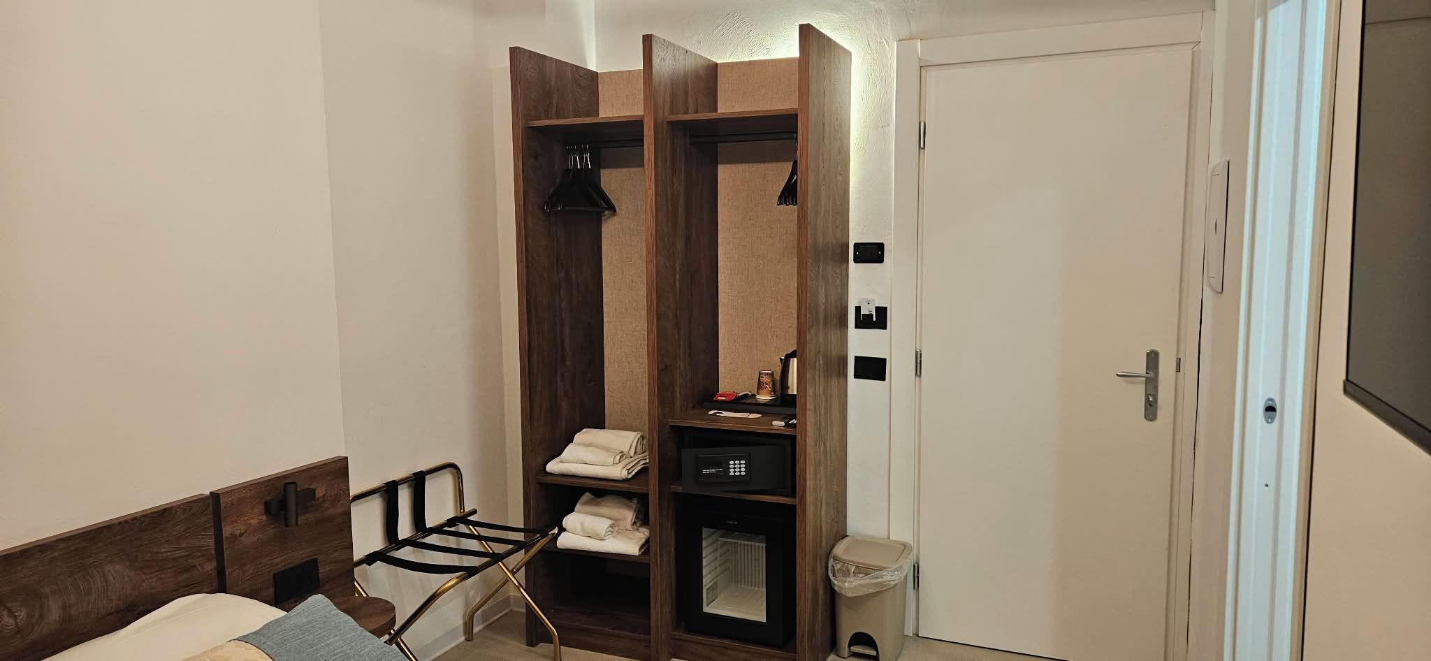 A compact room with a bed, a small seating area, a wardrobe, and a door.