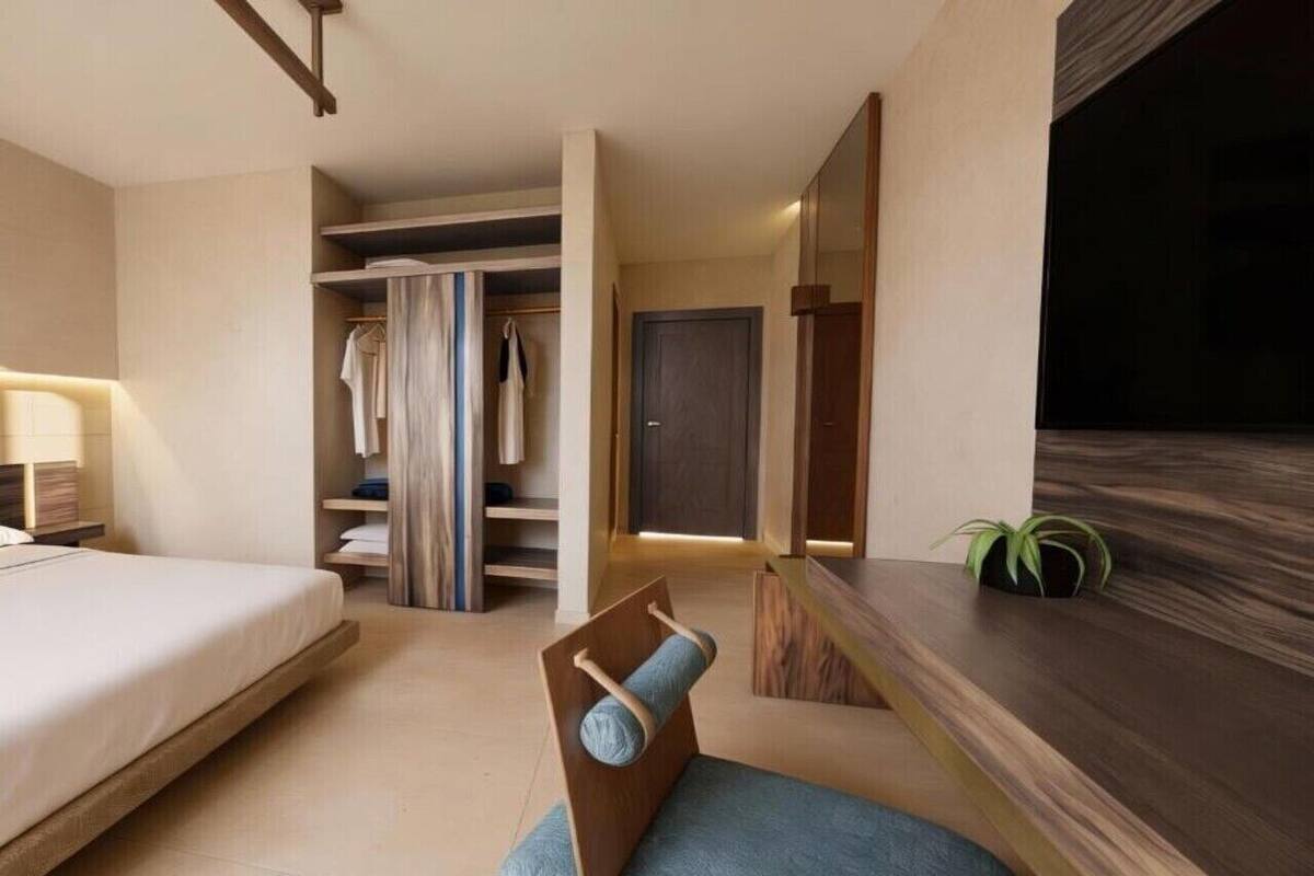 A modern hotel room with a bed, a seating area with a cushion, a wardrobe, and a small plant.