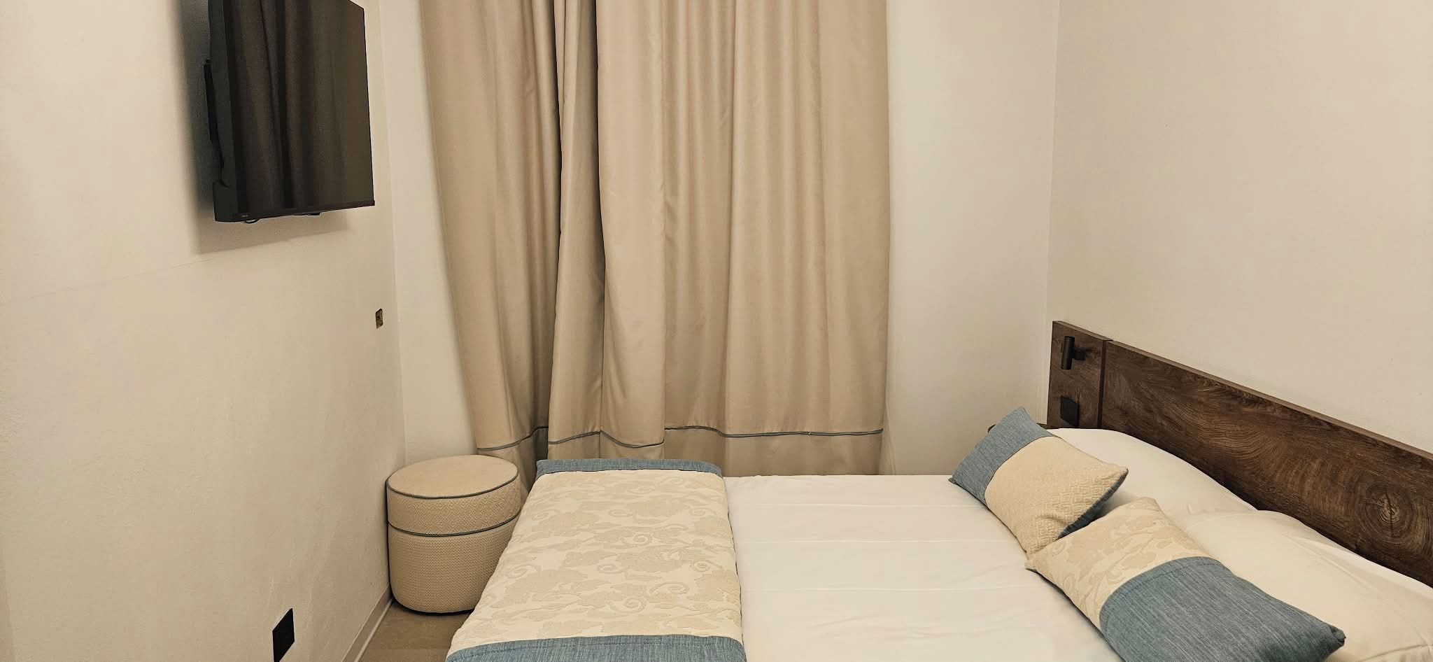A bedroom with a bed, curtains, a bedside table, and a wall-mounted TV.