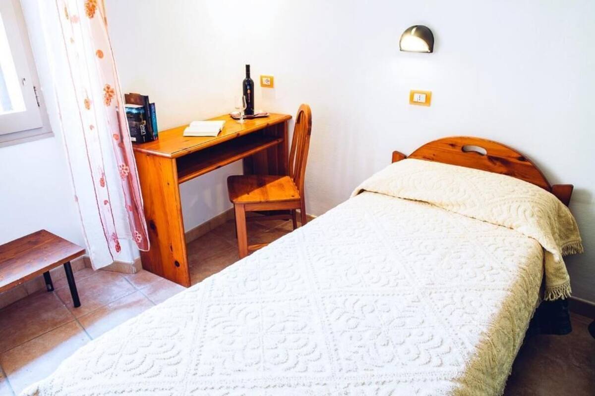 A bedroom with a bed, a wooden desk, a chair, and a bedside table.