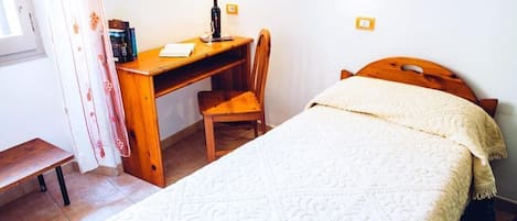 Een slaapkamer met een bed, een houten bureau, een stoel en een nachtkastje.
