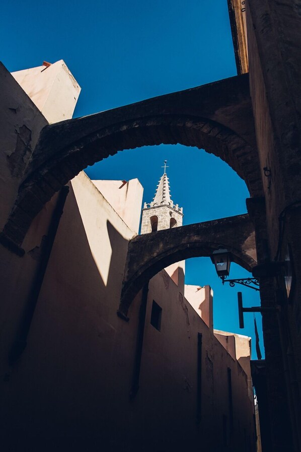 Uma estrutura de pedra em arco numa rua estreita, com uma torre ao fundo.