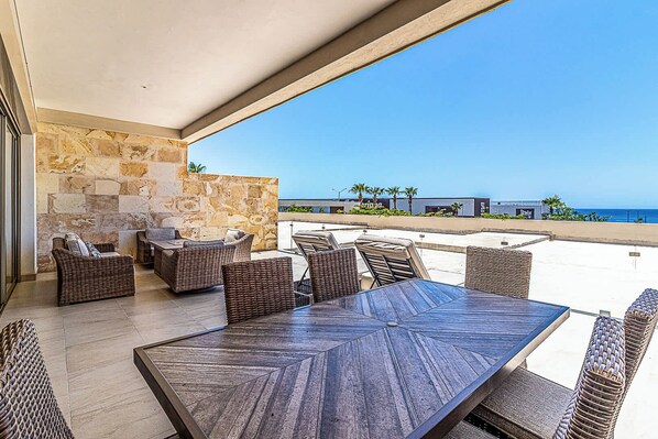 A terrace with wicker furniture, a stone wall, and a view of the ocean.