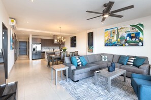 A modern living room with a grey sectional sofa, a coffee table, and a dining area in the background.