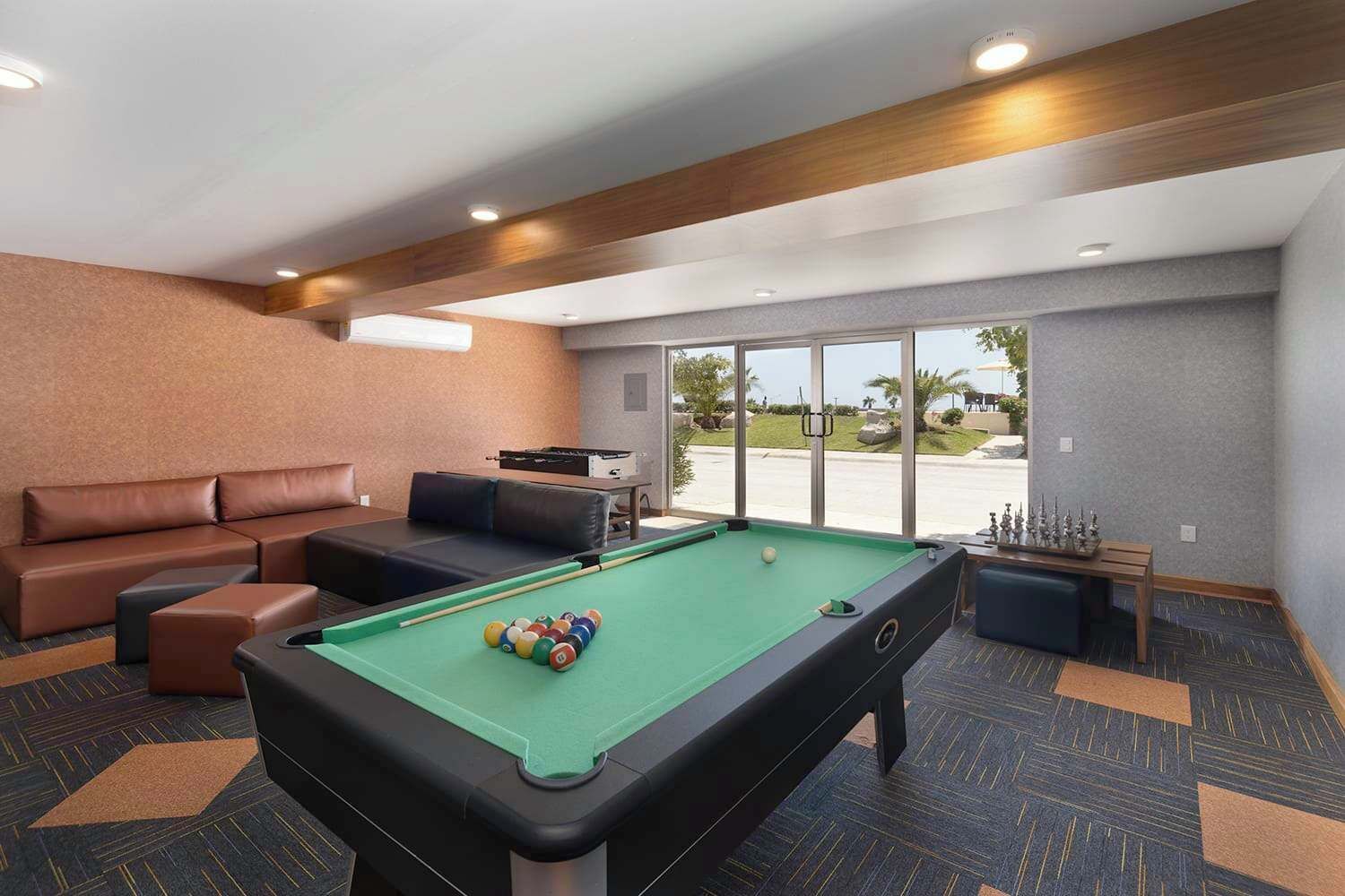 Een pooltafel met ballen, een bank en een biljarthouder in een kamer met vloerbedekking en uitzicht door een glazen deur.