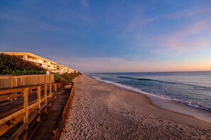 Una spiaggia con una passerella in legno, un edificio con diversi balconi e un cielo sereno.