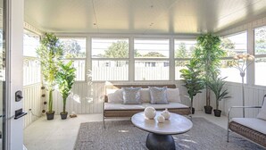 Une pièce baignée de lumière, avec un canapé en osier, une table ronde sur laquelle sont posées des théières et des plantes en pot.