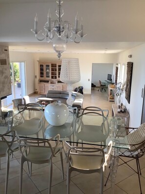 A spacious dining area with a glass table and chairs, a chandelier, and a cabinet with glass doors.