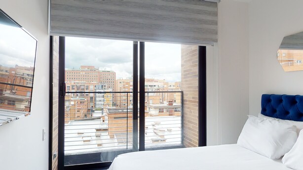 Une chambre d’hôtel avec une grande fenêtre, un lit avec une literie blanche et une tête de lit bleue.