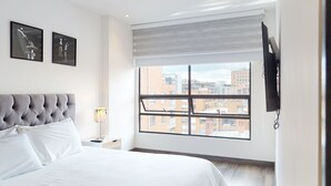 Une chambre d’hôtel moderne avec un grand lit, une vue sur la ville et des œuvres d’art accrochées au mur.
