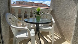 A small outdoor balcony with a round glass table and two white plastic chairs.
