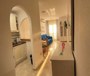 A narrow hallway leading to a kitchen and living area with a blue sofa and a dining table. - Godisa 18 Apartment Playa del Cura Torrevieja! (Torrevieja)