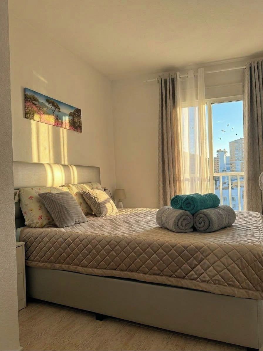Hotellihuone, jossa on sänky, taulu seinällä ja ikkuna, jossa on verhot.