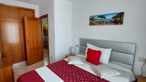A bedroom with a bed, a nightstand, a lamp, a painting, and a wooden wardrobe.