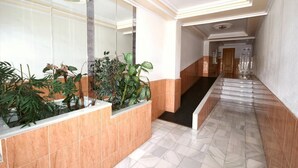 A hallway with a marble floor, a glass wall with plants, and a staircase leading to another area.