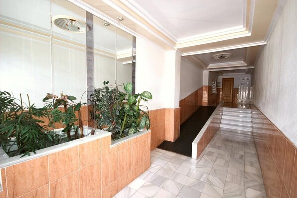 Un pasillo con piso de mármol, una pared de vidrio con plantas y una escalera que lleva a otra zona.