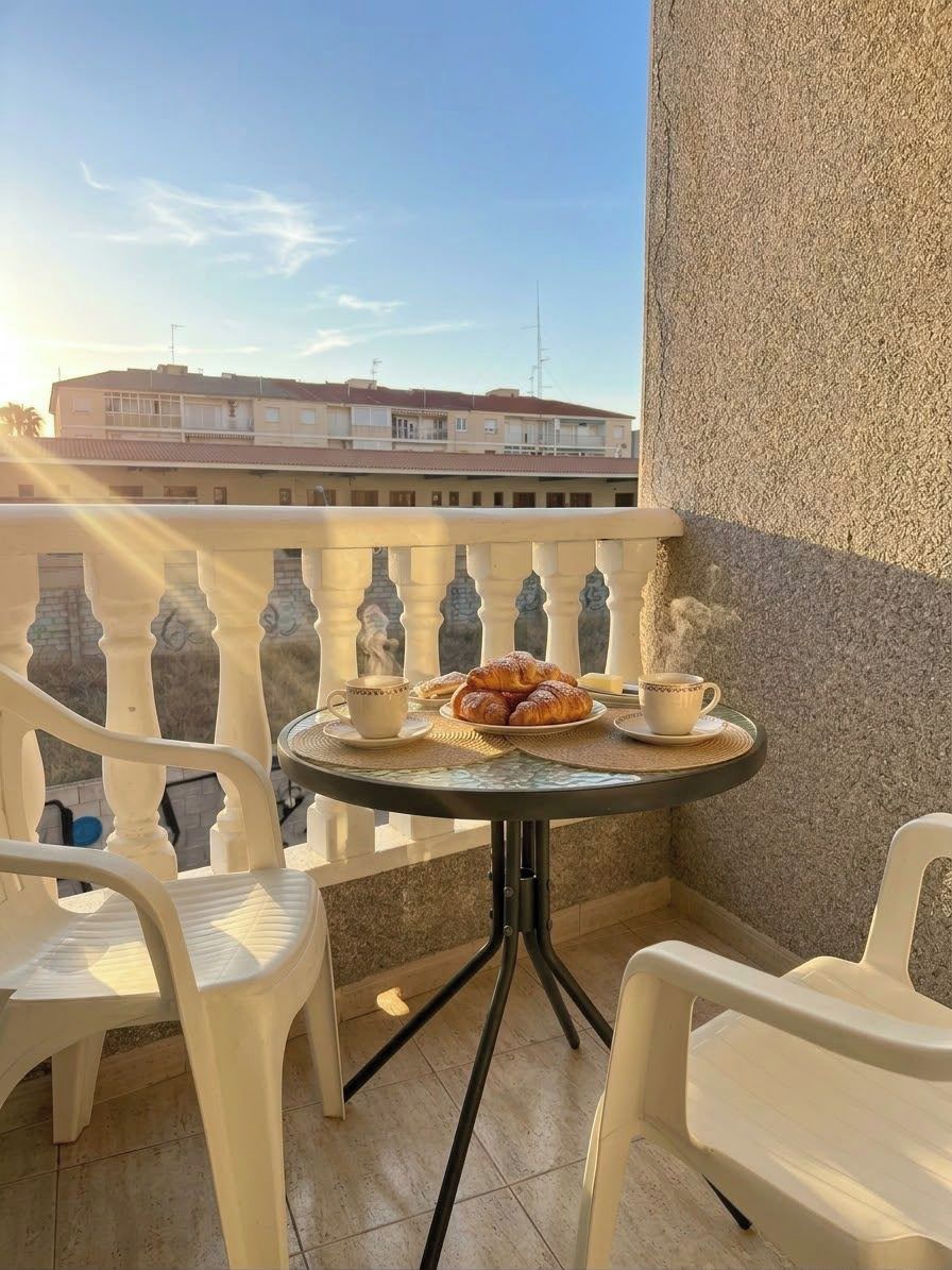 A balcony with a table set for breakfast, including croissants and a cup, with chairs around.