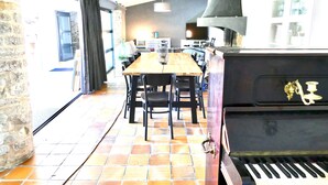 A dining area with a wooden table and chairs, a piano, and a kitchen in the background.