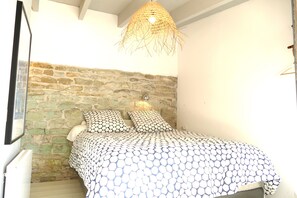 Une chambre avec un mur en pierre, un lit avec une literie à motifs et un luminaire suspendu.