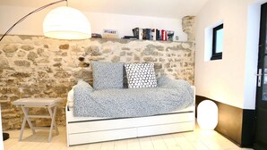 A cozy room with a stone wall, a white sofa with patterned cushions, a small wooden table, and a hanging light fixture.