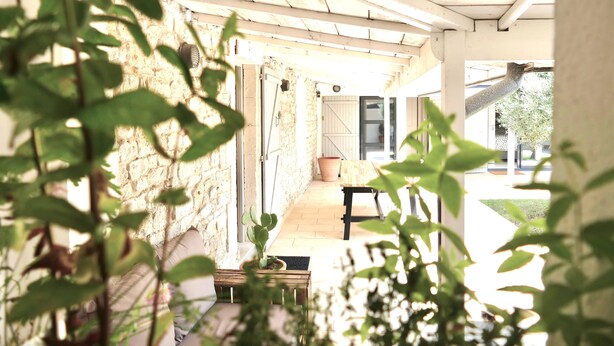 A covered porch with a stone wall, a wooden bench, and a potted cactus.