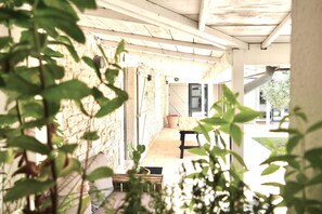 Une véranda couverte avec un mur en pierre, un banc en bois et un cactus en pot.