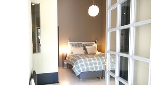A bedroom with a bed, bedside table, lamp, and a window with white frames.