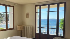 A bedroom with a bed, a chair, a radiator, and a view of the sea through large windows. - Villa " La plage "  waterfront villa, swimming pool, garden, 16 p (Carqueiranne)