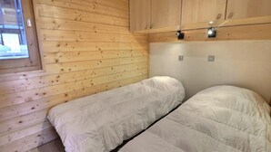 Uma cabana pequena, com um único quarto, paredes de madeira e uma janela. Há duas camas com roupa de cama branca.