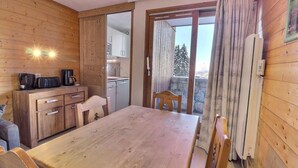Interior em madeira com mesa de jantar, cadeiras, área de cozinha e vista para árvores por uma porta deslizante.