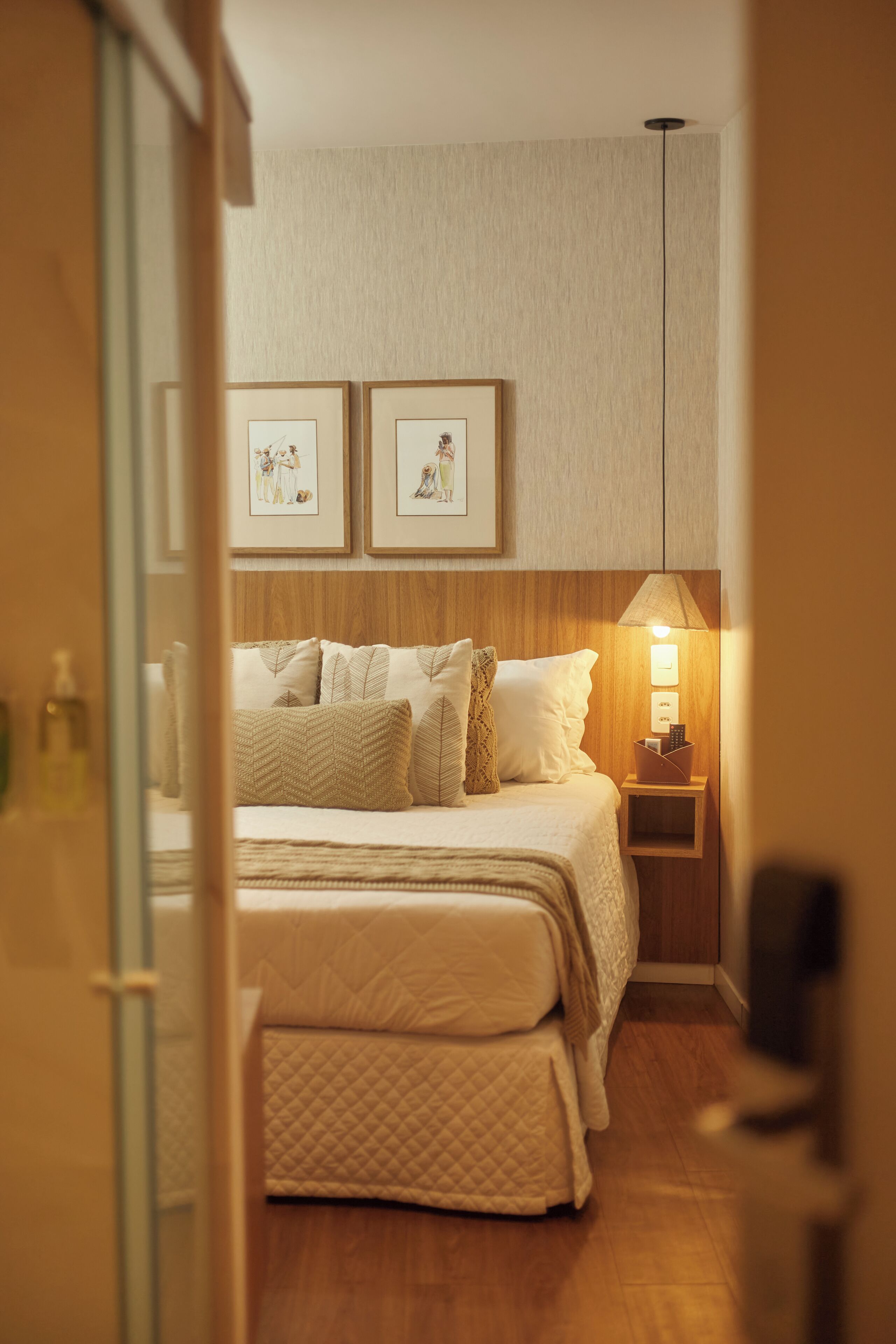 Un dormitorio ordenado con cama, mesita de noche y cuadros colgados en la pared.