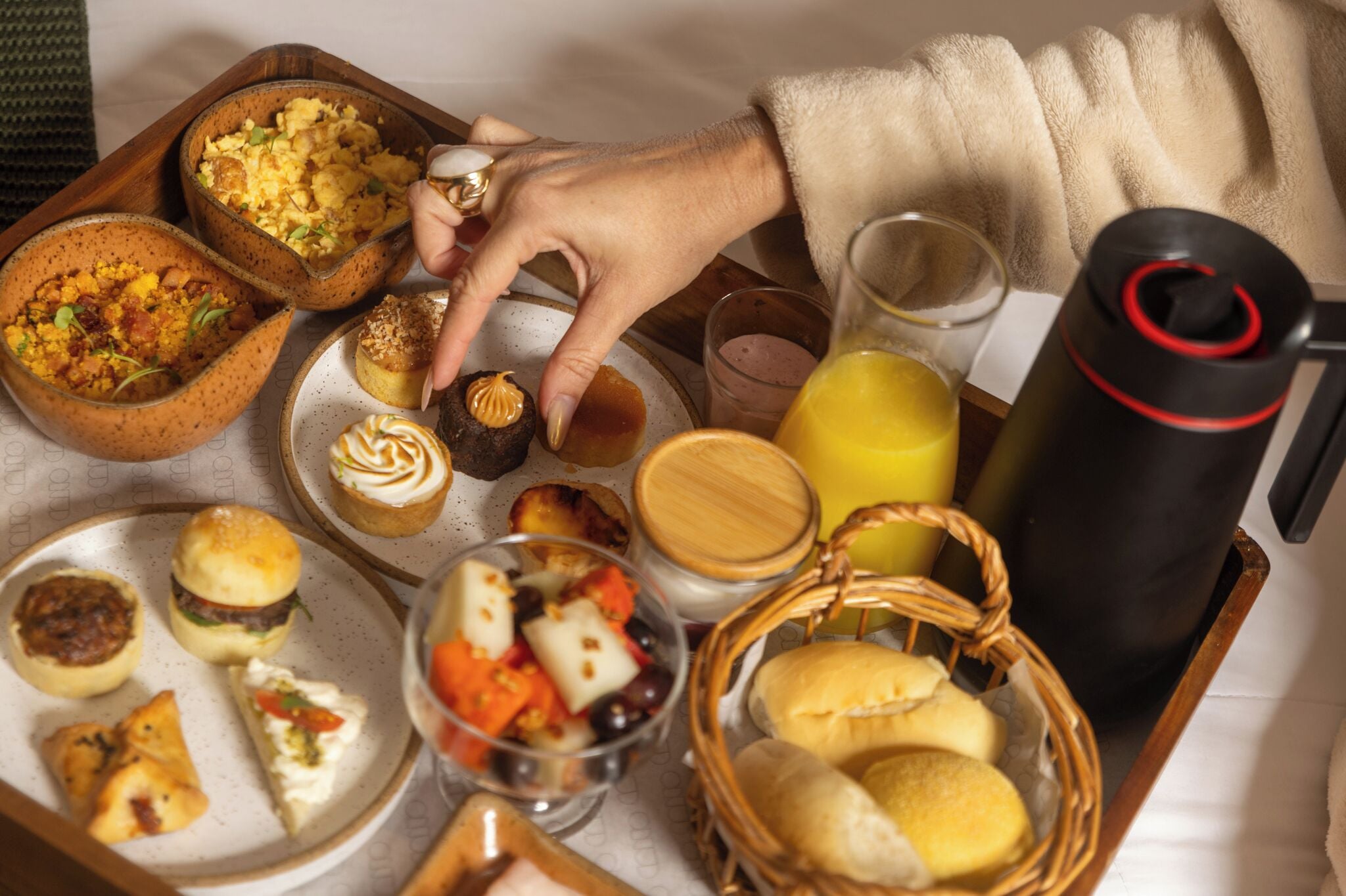 A breakfast tray with various pastries, a glass of orange juice, and a thermos.