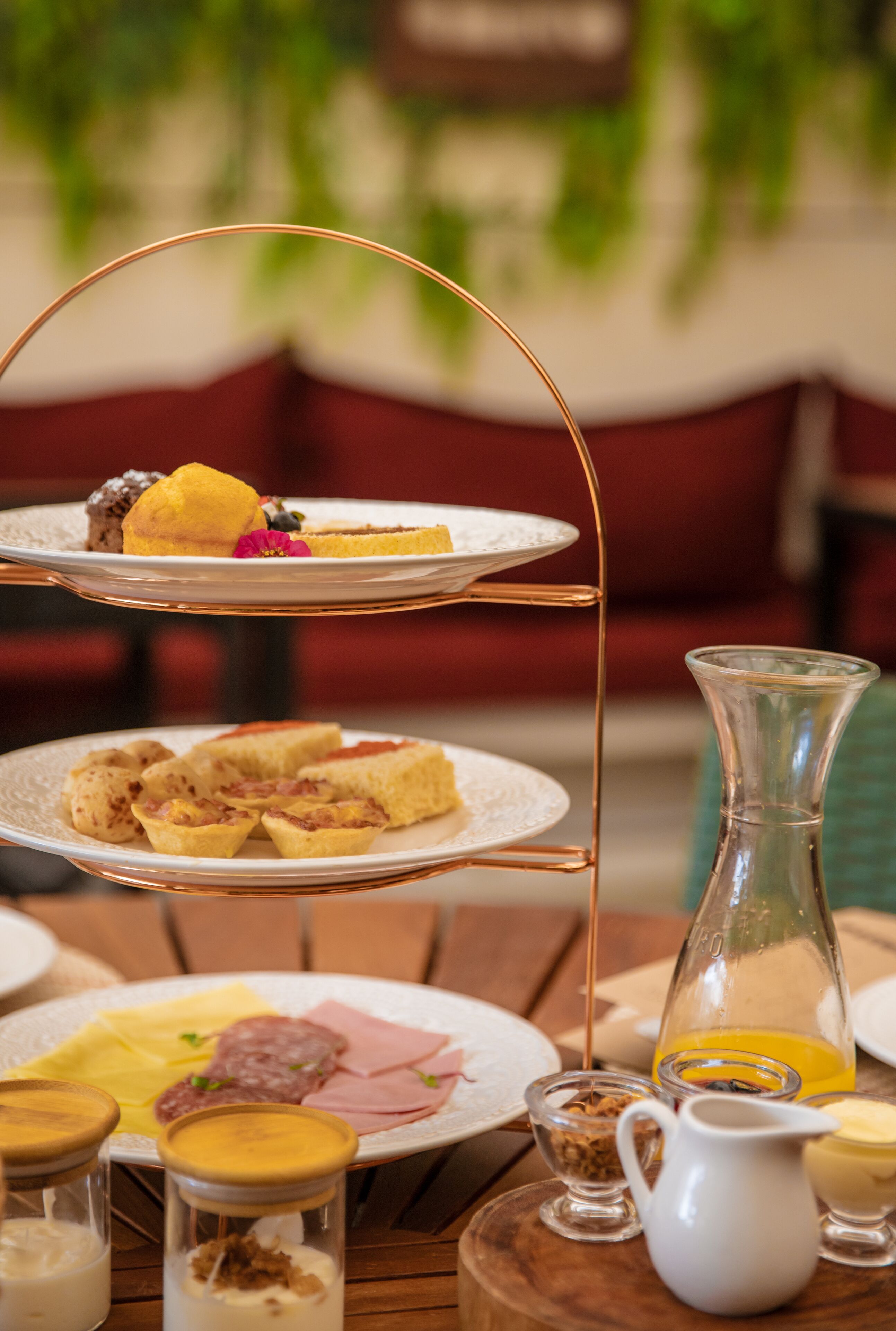 A tiered serving tray with various pastries and a glass pitcher on a wooden table.