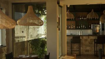 A restaurant with wooden tables and chairs, hanging wicker lamps, and a bar area with shelves of bottles.