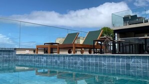 Ein klares, blaues Schwimmbecken mit gefliesten Rändern, Liegestühlen und einem Glasgeländer.