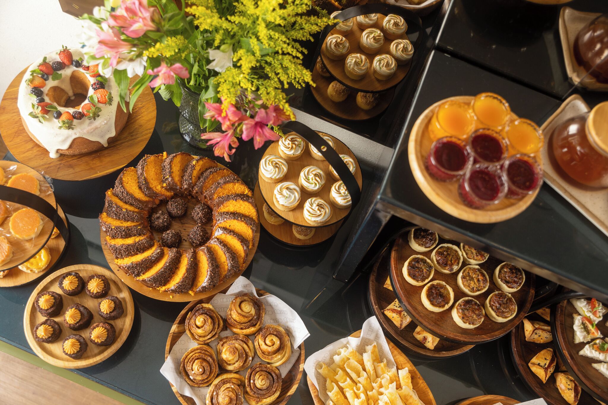 Ett varierat urval av desserter och bakverk på ett buffébord, inklusive en sockerkaka, muffins och fruktpajer.