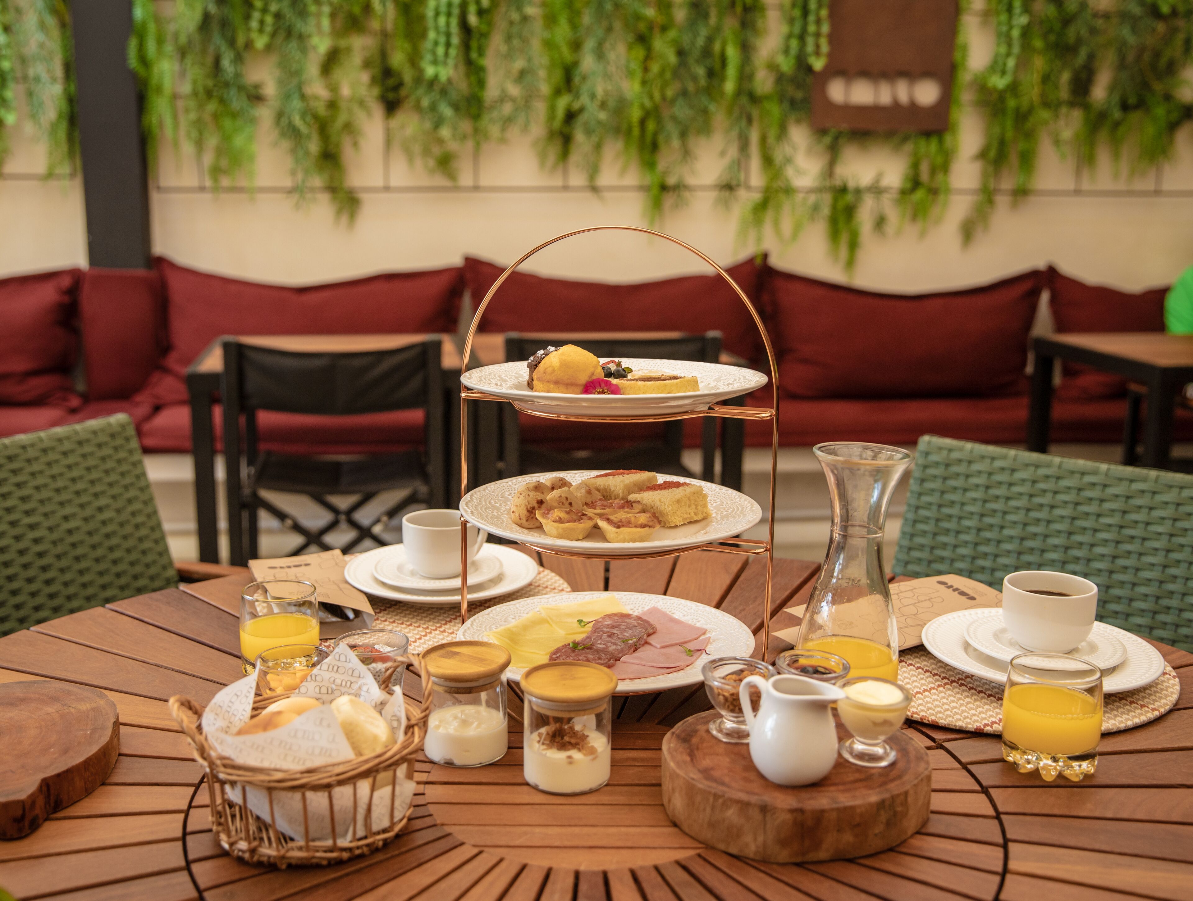 Une table en bois dressée pour le petit-déjeuner, avec un plateau à étages servant de présentoir, des assiettes remplies de nourriture et diverses boissons.