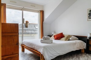 A bedroom with a bed, a wooden wardrobe, a nightstand, and a window with curtains. - Epicea- Spacieux 3 chambres avec parking (Nantes)