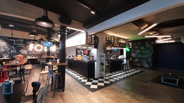 Una cafeteria moderna amb una zona de bar, un terra de pissos escacs i obra d'art a la paret.