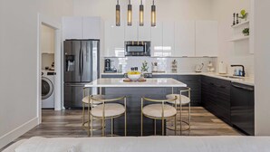 Une cuisine moderne dotée d’un îlot central, d’appareils électroménagers en acier inoxydable et de luminaires suspendus.
