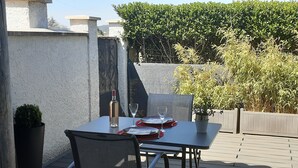 An outdoor patio with a table set for two, a bottle of wine, and a glass.