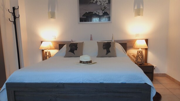 A neatly made bed with a white comforter and two pillows, a hat on the bed, and two bedside lamps on either side.