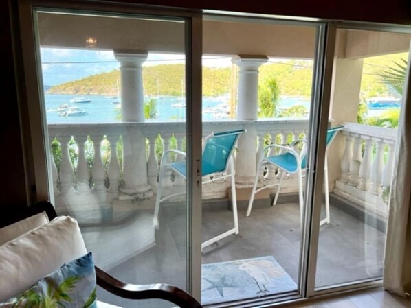 A balcony with a view of a pool and boats, white chairs, and a glass door.