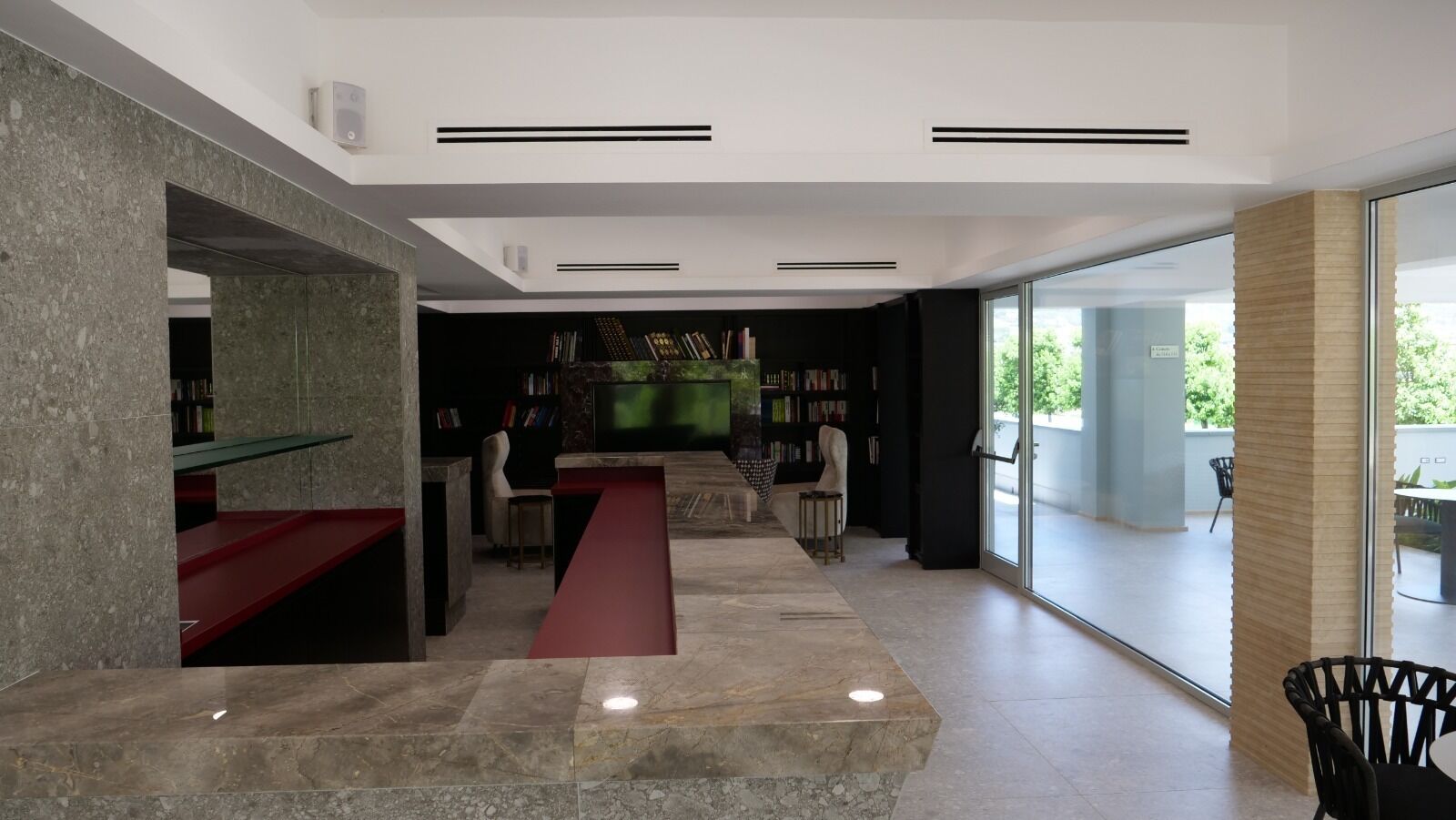 A modern interior with a stone reception desk, a red bench, and a bookshelf.