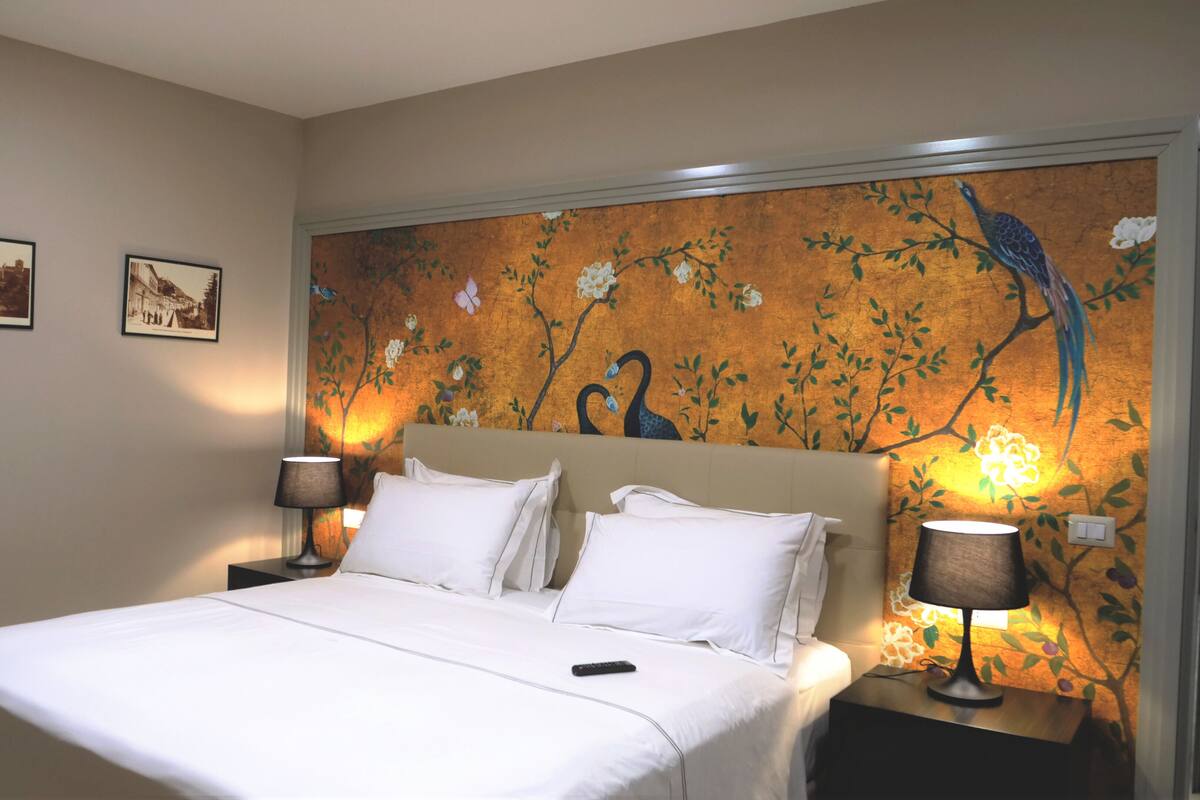 A hotel room with a large bed, two bedside lamps, and a wall mural of birds and flowers.