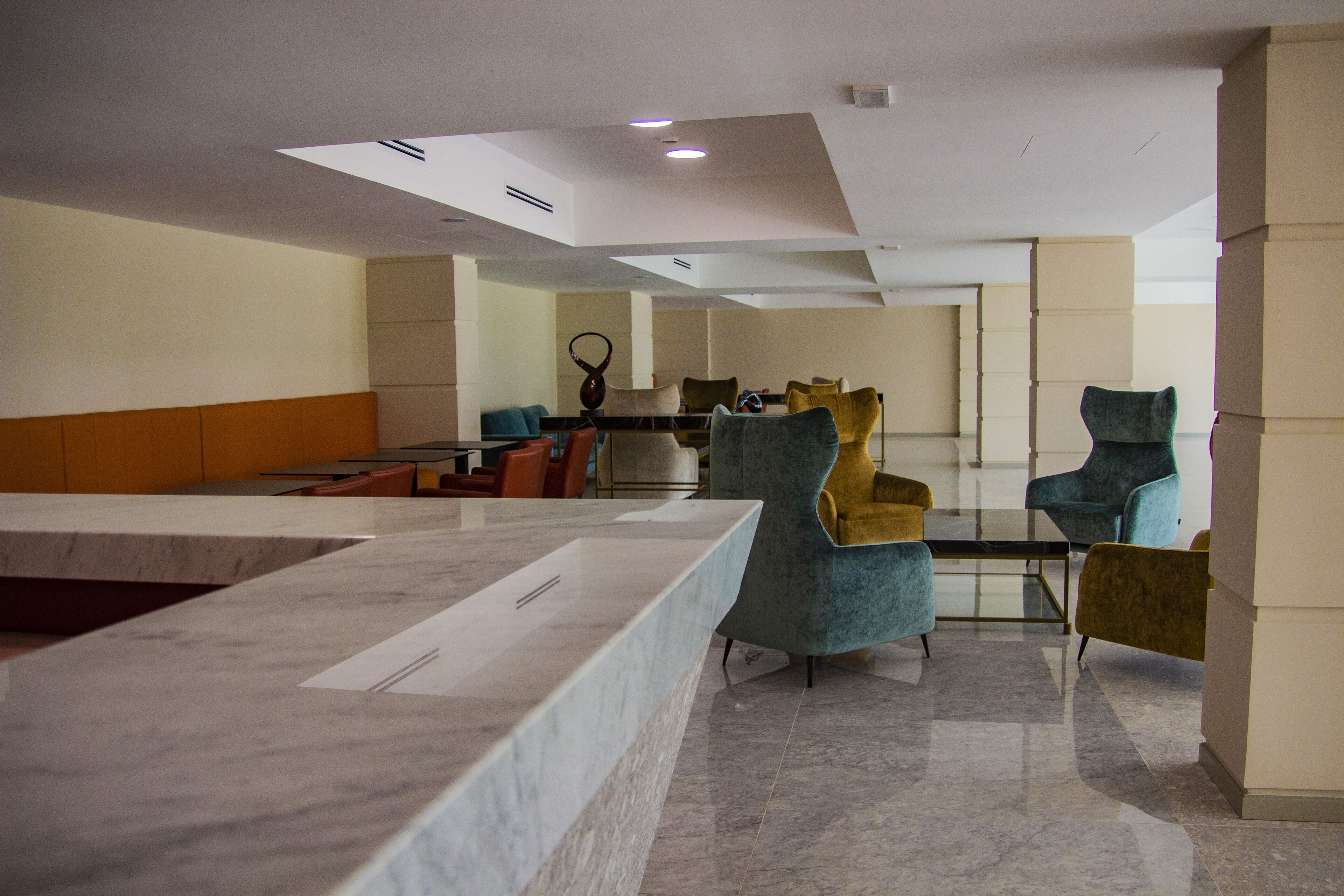 Un hall d’entrée moderne avec un comptoir de réception en marbre, des espaces de détente confortables et un grand miroir.