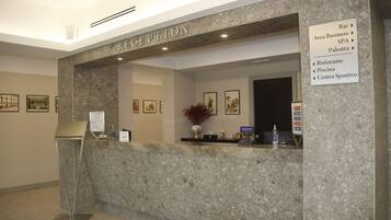 Een receptie met een marmeren balie, een receptiebalie, ingelijste kunstwerken aan de muren en een bord waarop de faciliteiten van het hotel staan.